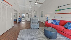 Ein geräumiges Wohnzimmer mit einem roten Sofa, einem gemusterten Sessel und einem Hocker, Holzboden und Deckenventilator.