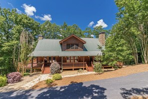 A log cabin with a green metal roof, wooden deck, and a stone pathway leading to the entrance.