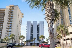 A multi-story building with balconies, palm trees, and parked cars.