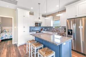 A modern kitchen with white cabinets, a stainless steel refrigerator, and a blue island with stools.