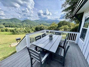 Een houten terras met een tafel en stoelen, met uitzicht op een groen landschap met heuvels.