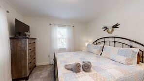 Een slaapkamer met een bed, een dressoir, een raam met gordijnen en een decoratie aan de muur.