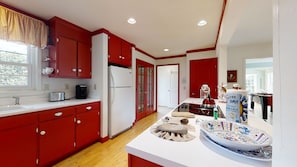 Une cuisine moderne avec des meubles de rangement rouges, un plan de travail blanc et un îlot central agrémenté d’objets décoratifs.