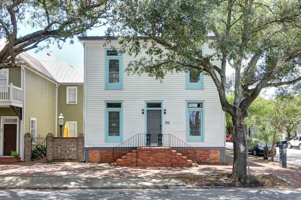 A two-story house with a front porch, a brick base, and a tree in front.