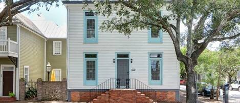 A two-story house with a front porch, a brick base, and a tree in front.