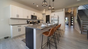 A modern kitchen with white cabinets, a central island with bar stools, stainless steel appliances, and pendant lighting.