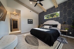 Un dormitorio moderno con una cama grande, ventilador de techo, ventana con vista a follaje y un diseño de pared original.