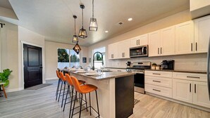 A modern kitchen with a central island, bar stools, white cabinets, and pendant lighting.