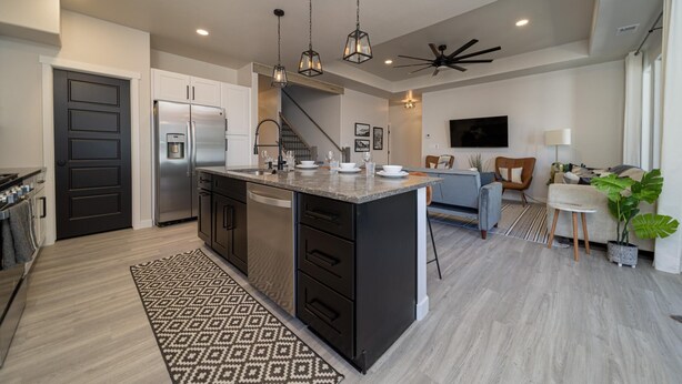 A modern kitchen with a central island, stainless steel appliances, pendant lighting, and a ceiling fan.