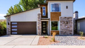 A modern two-story house with a garage, stone facade, and a small garden area.