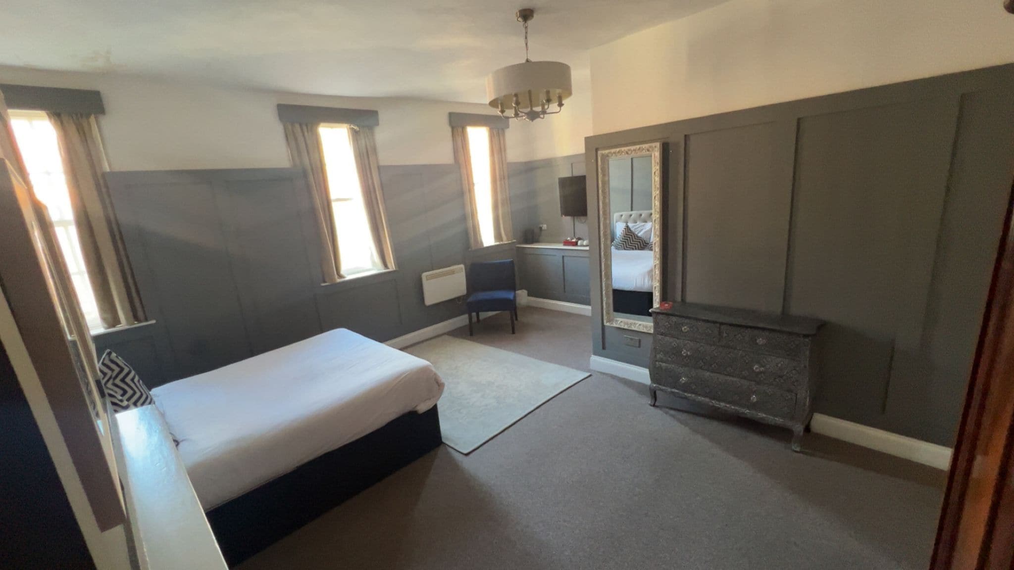 A bedroom with a bed, a dresser, a chair, a mirror, and a window.