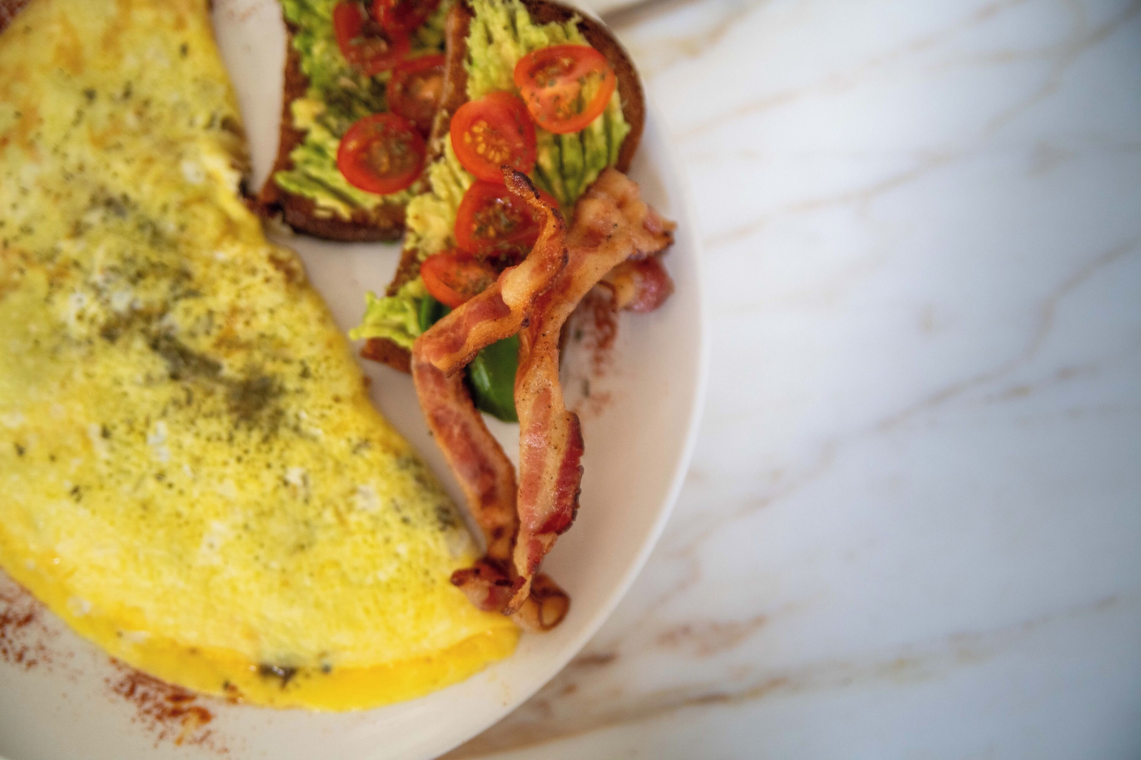 En tallerken med omelet, bacon, salat og tomatskiver.