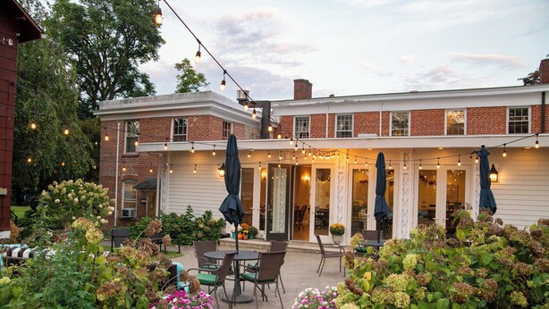A brick building with a covered patio area featuring outdoor seating and string lights. - Cromwell Manor Inn (Cornwall)
