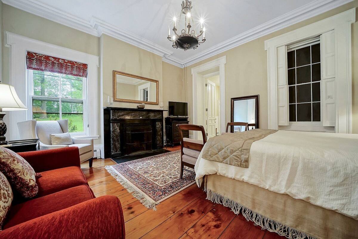 A spacious room with a large bed, a fireplace, a television, and a view of the outdoors.
