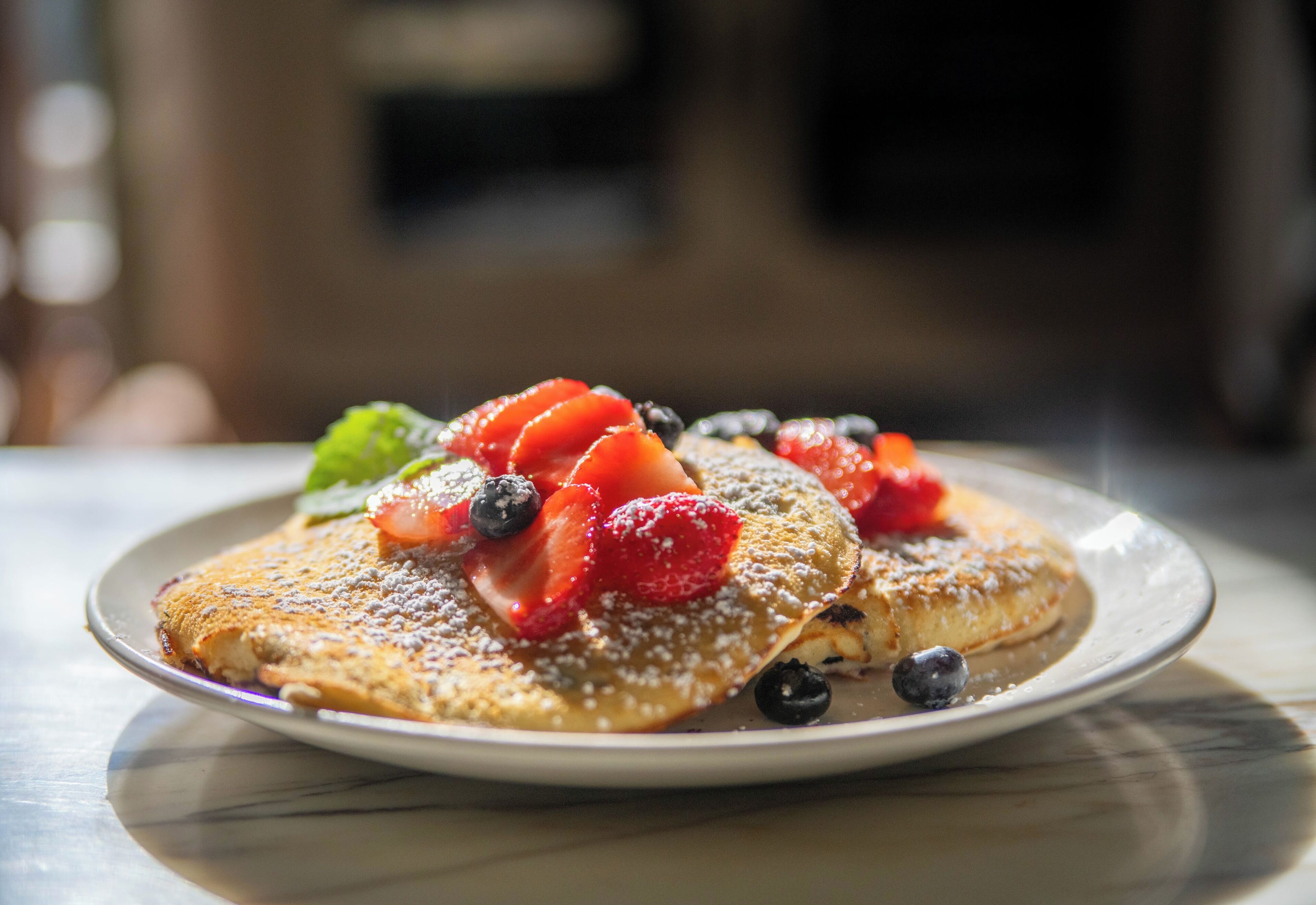 A plate of pancakes topped with strawberries, blueberries, and a mint leaf.