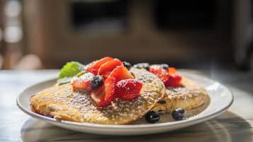 A plate of pancakes topped with strawberries, blueberries, and a mint leaf.