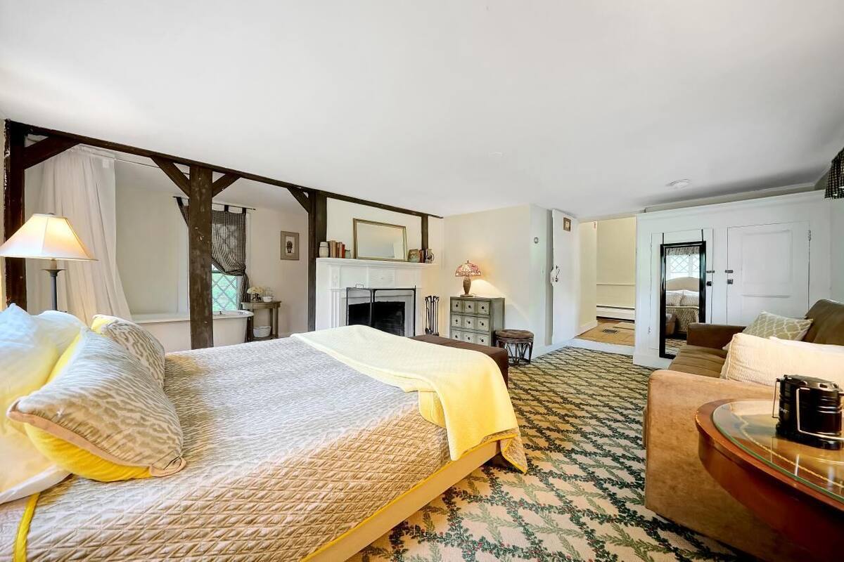 A hotel room with a bed, a sitting area with a table and chairs, a fireplace, and a mirror.