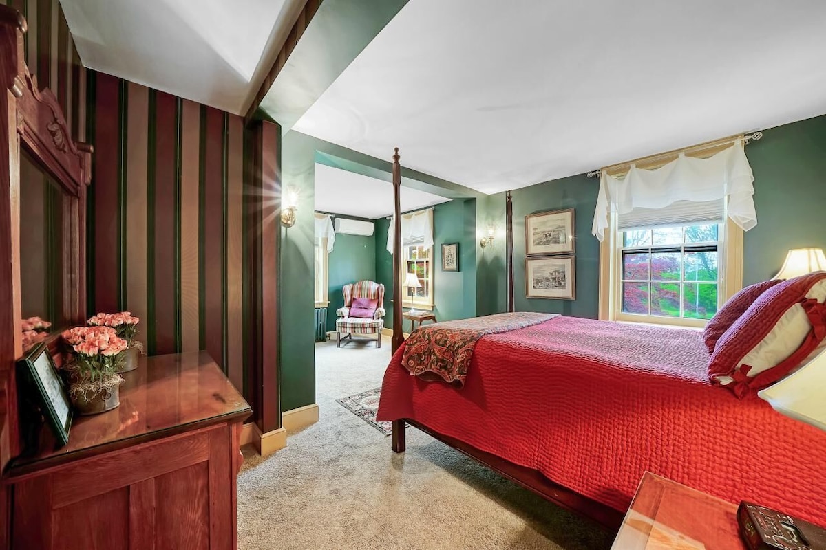 Een slaapkamer met een groot bed, een houten dressoir, een stoel en een raam met gordijnen.