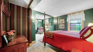 A bedroom with a large bed, a wooden dresser, a chair, and a window with curtains.