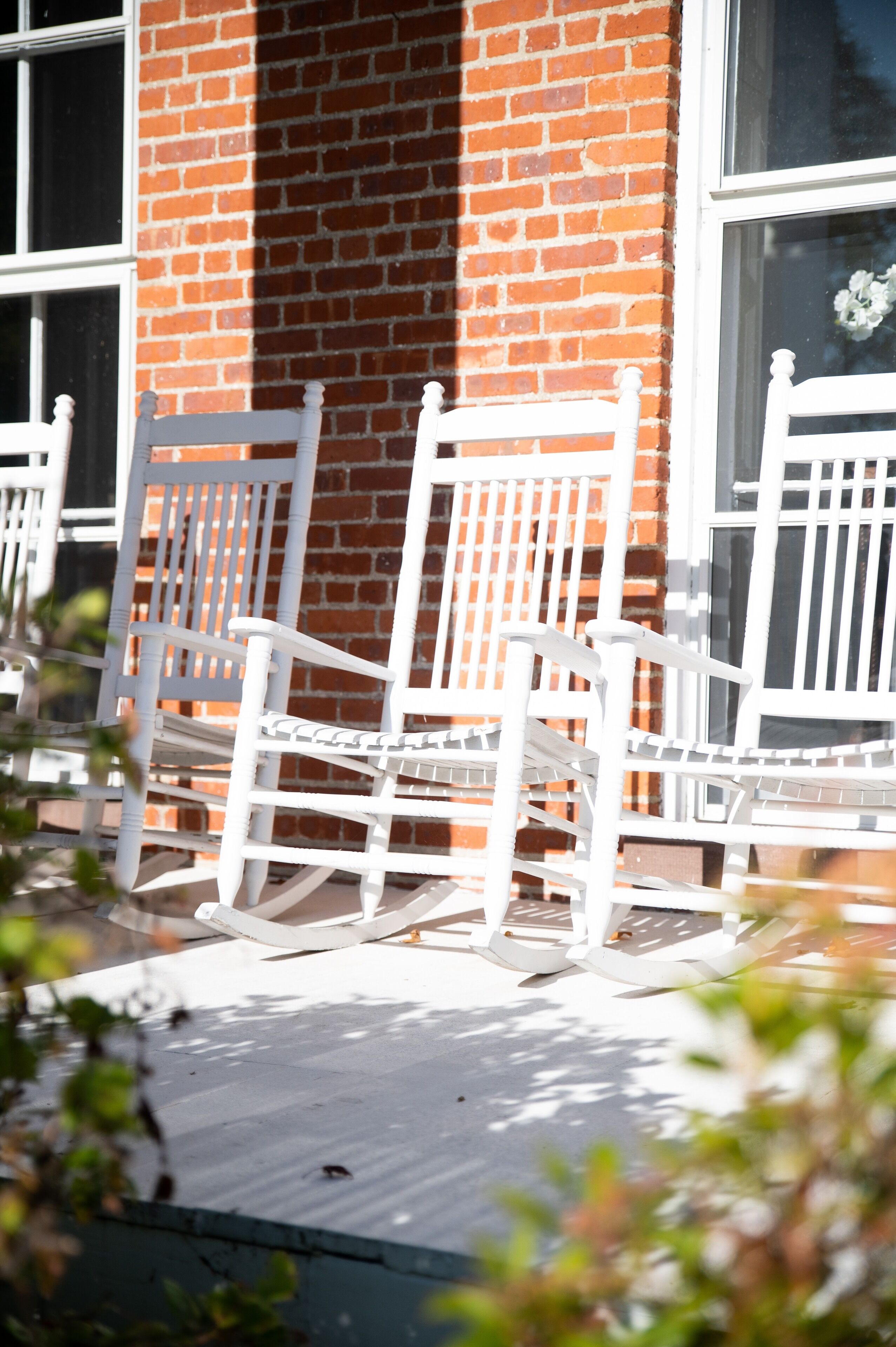White rocking chairs on a wooden deck in front of a brick building with large windows.