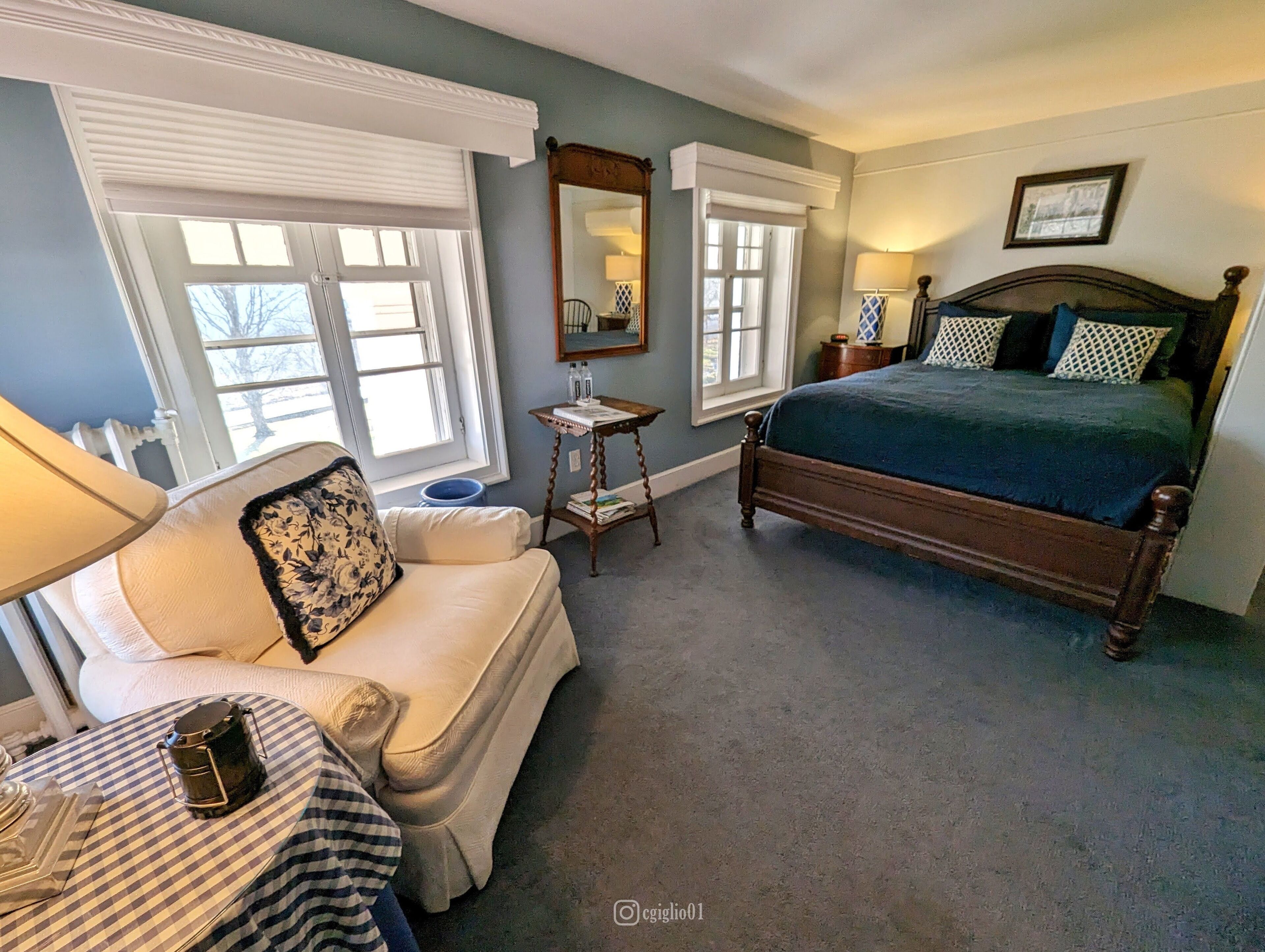 A bedroom with a bed, a sofa, a small table, and a lamp.