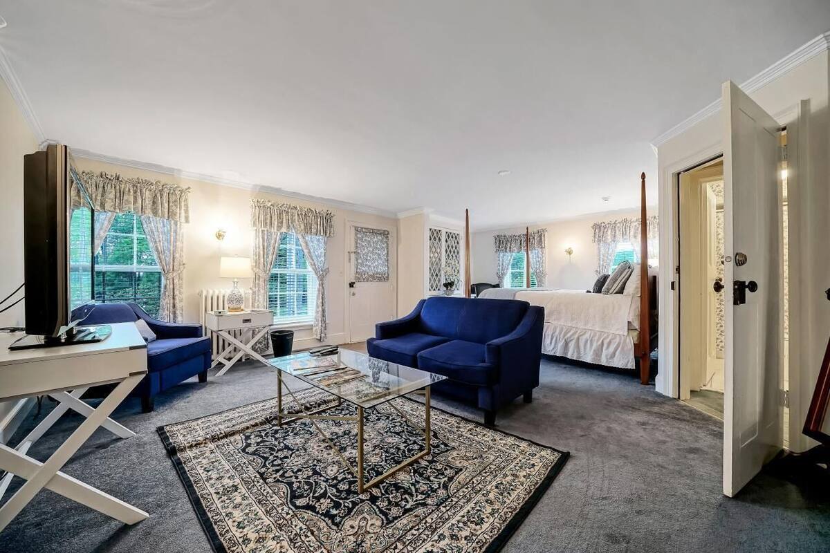 A spacious living room with a large window, a sofa, a coffee table, and a bed.