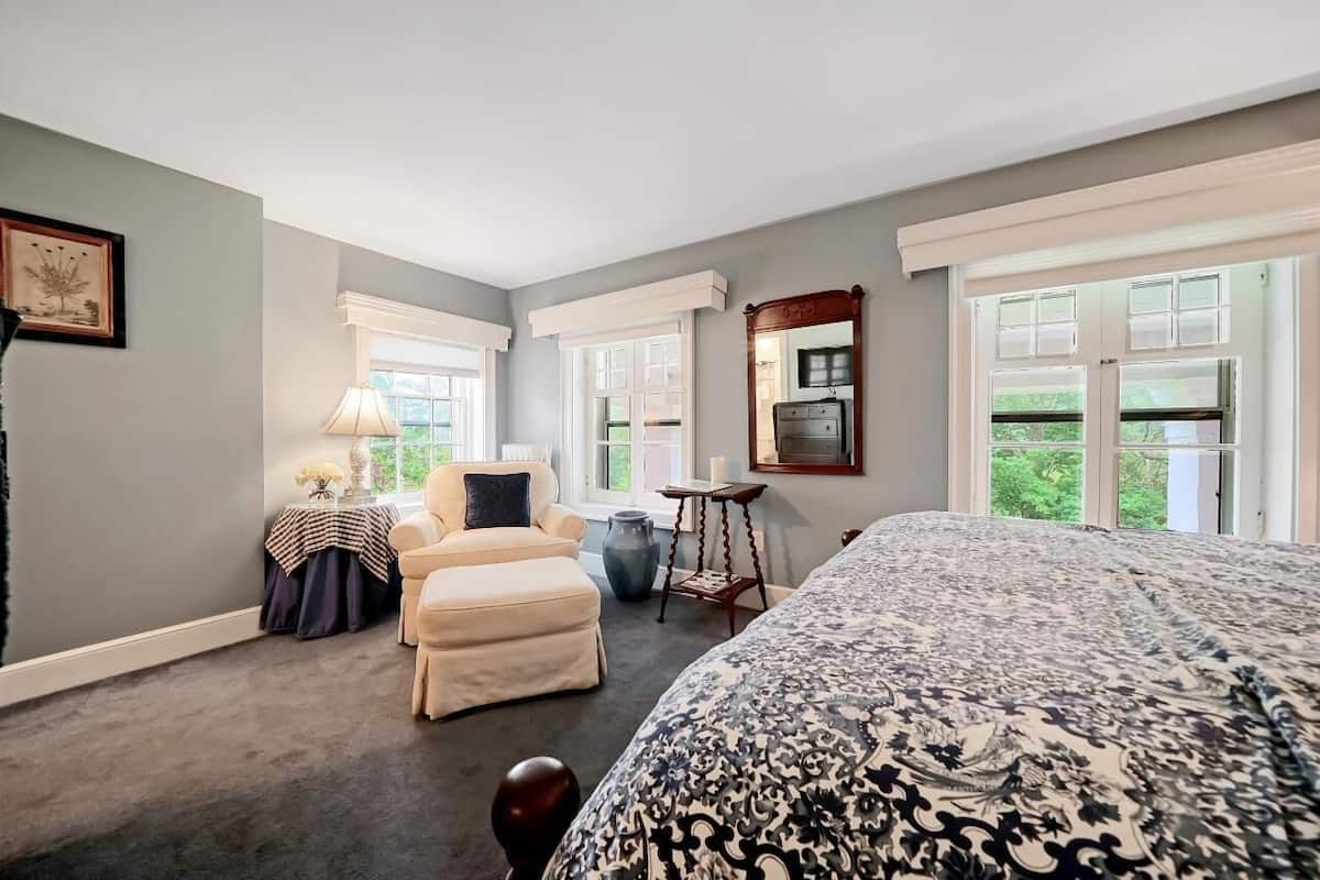 A bedroom with a large bed, a chair, a table, and a mirror.