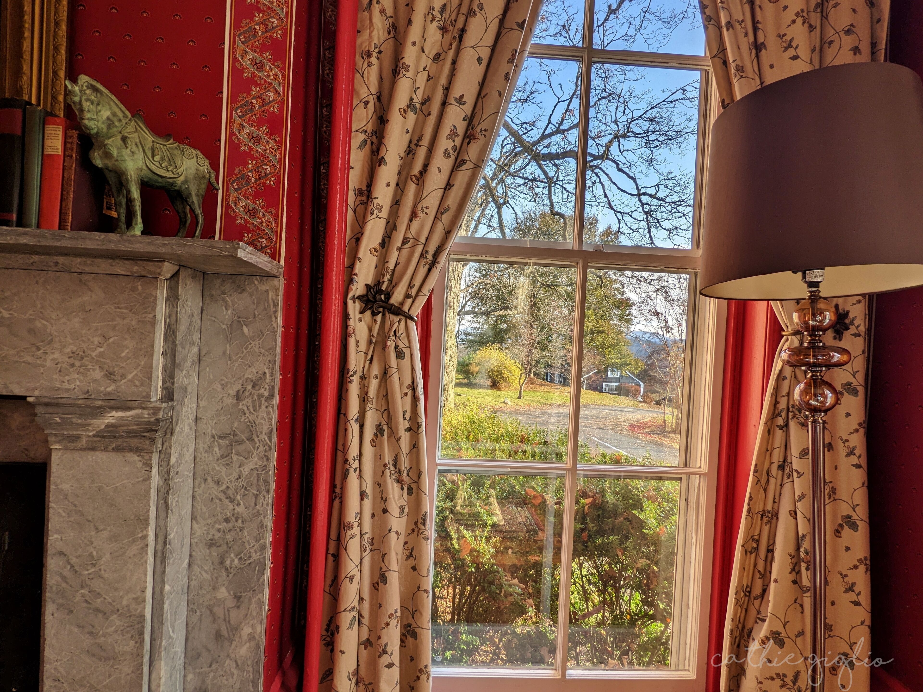 Een kamer met een open haard, een raam met rode gordijnen, en een lamp.