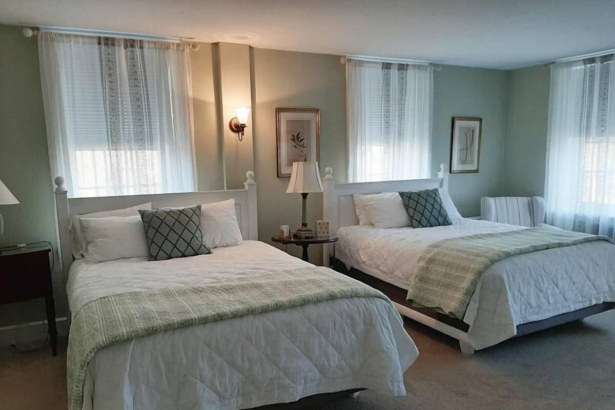 A hotel room with two beds, a nightstand, a lamp, and a framed picture on the wall.