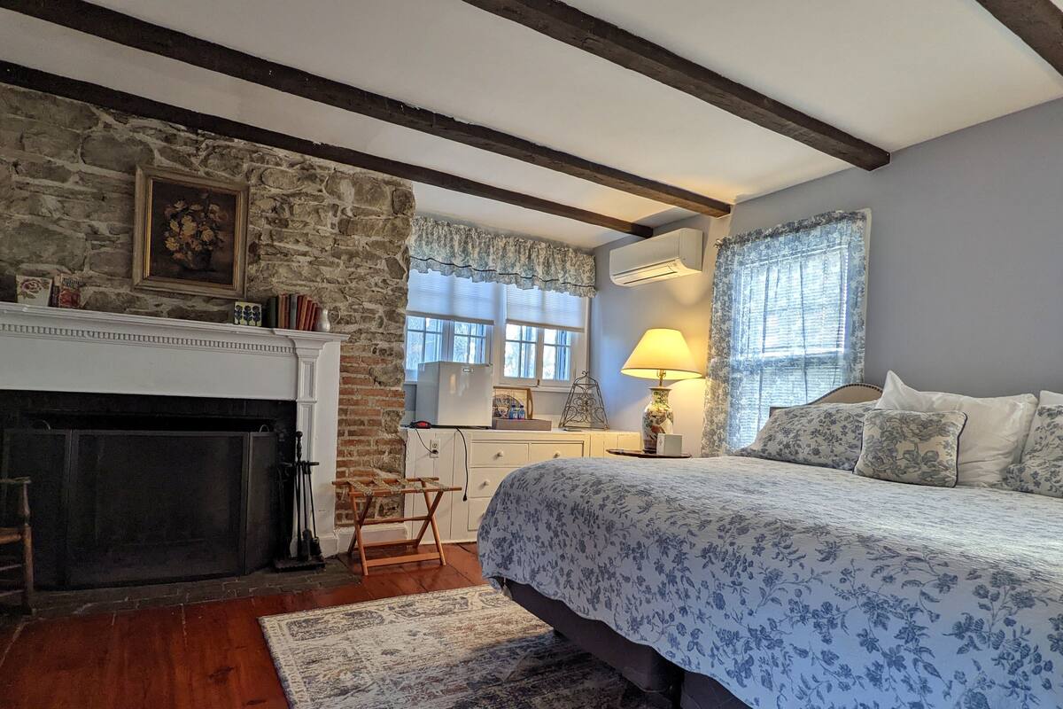 A bedroom with a stone wall, a fireplace, a bed with floral bedding, and a nightstand with a lamp.