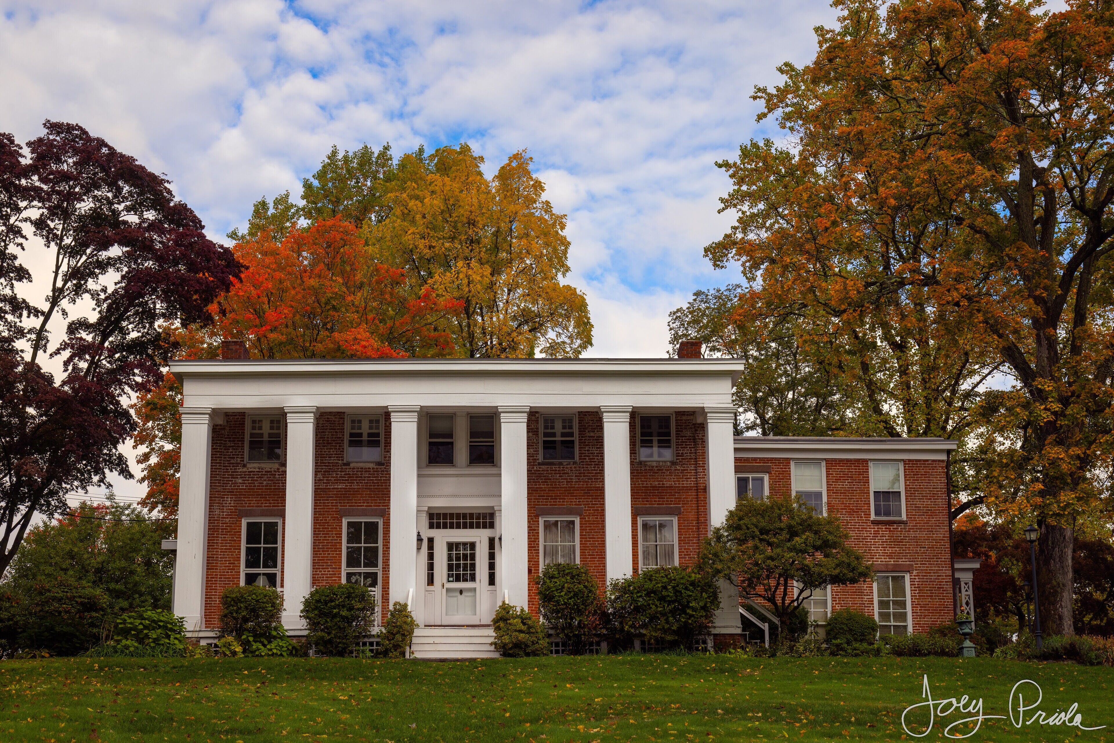 A large, two-story brick building with a central entrance flanked by columns, surrounded by a well-maintained lawn and autumn-colored trees.