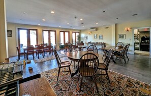 A spacious dining area with multiple tables and chairs, large windows, and a kitchen area visible in the background.