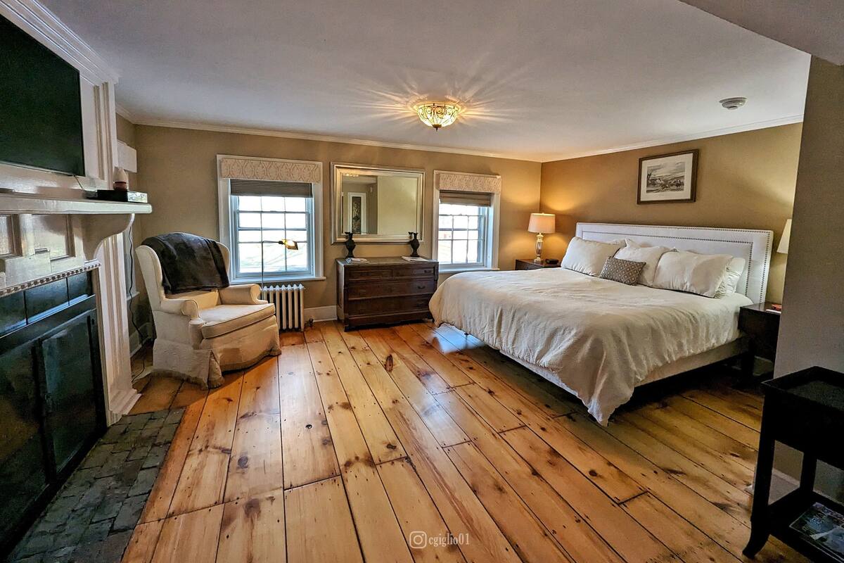 A bedroom with a large bed, a dresser, a chair, a mirror, and a fireplace.