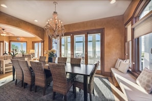 A dining area with a large table and wicker chairs, a chandelier, and large windows with blinds. - Welcome to Hidden Gem this stunning beachfront home is located in the gated community of the Plantation. Boasting 5 bedrooms and 5 bathrooms this home is perfect for large families that enjoy their own space. (St. George Island)