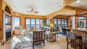 A spacious living room with a fireplace, comfortable seating, a bar area, and large windows offering ocean views.
