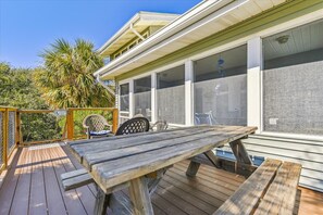 A wooden deck with a picnic table, chairs, and a covered area with large windows. - Welcome to Daddy’s Money! (St. George Island)
