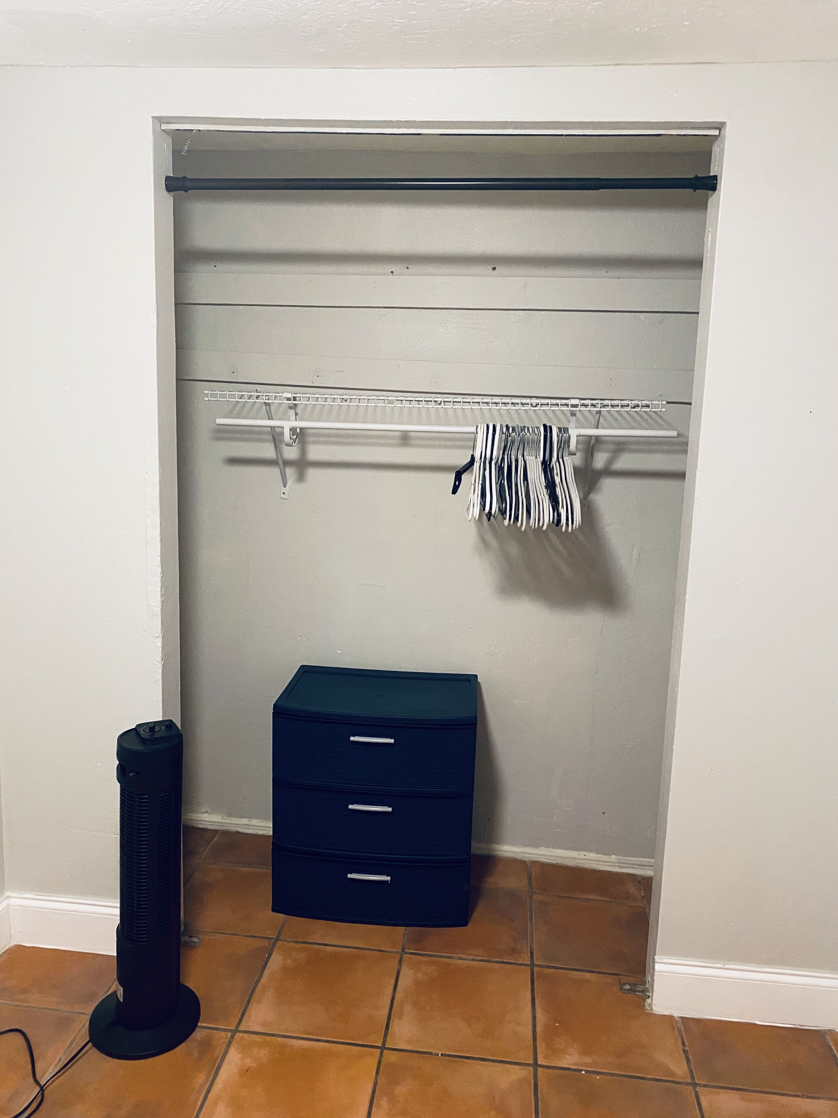 A closet with a hanging rod, a storage box, and a floor fan.