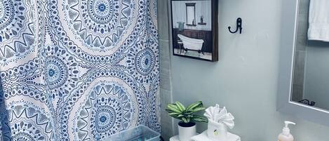 A bathroom with a patterned shower curtain, a toilet, a sink with a mirror, and a shelf with towels.