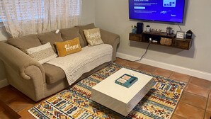 Un salon avec un canapé marron, des coussins à motifs, un plaid blanc, une table basse surmontée d’une boîte décorative, un tapis coloré et un téléviseur à écran plat fixé au mur.