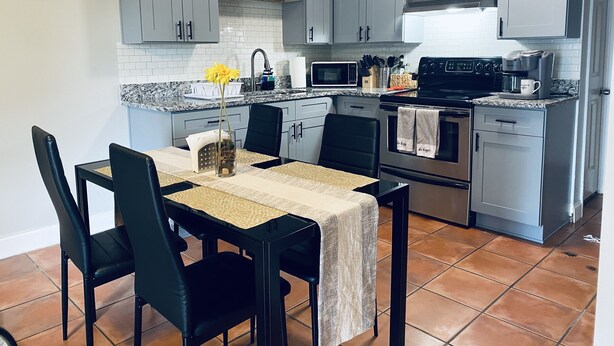 Une cuisine moderne avec des meubles gris, un plan de travail noir et un coin repas comprenant une table et des chaises.