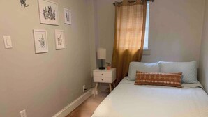 Une chambre à coucher avec un lit, une table de chevet, une lampe et des reproductions botaniques encadrées accrochées au mur.