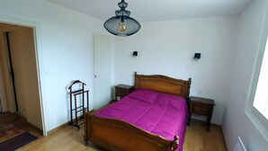A bedroom with a wooden bed, a purple bedspread, two bedside tables, a nightstand, a hanging light fixture, and a door. - Ty - Néhué (Crac'h)