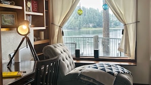 Une pièce chaleureuse avec vue sur un lac, un fauteuil confortable, un bureau avec une lampe et une bibliothèque.