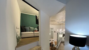 Een moderne woonkamer met een bank, een decoratieve wand en een trap naar een andere kamer.