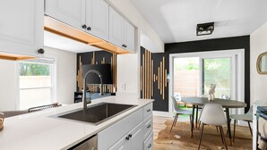 A modern kitchen with white cabinets, a black backsplash, and a dining area with a round table and chairs.