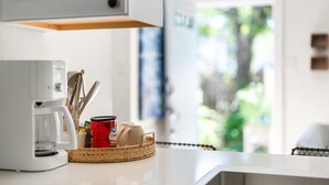 A kitchen counter with a coffee maker, a basket with utensils, and a red mug.