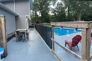 Ein Garten mit Swimmingpool, einer Holzterrasse und einem eingezäunten Bereich mit roten Stühlen.