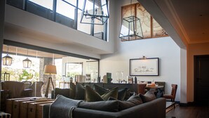 A spacious living area with a high ceiling, large windows, and a cozy seating arrangement. - Kruger National Elephant Point Lodge (Mbombela)