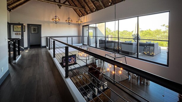 A spacious room with a high ceiling, large windows, and a balcony with outdoor seating. - Kruger National Elephant Point Lodge (Mbombela)