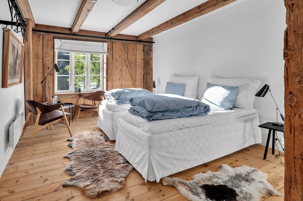 Un dormitorio con techo de madera, cama con ropa de cama blanca, alfombra de pieles y ventana con vistas a la vegetación.